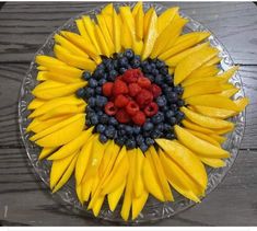 a clear plate topped with bananas, raspberries and blueberries on top of a wooden table