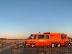 an orange van parked in the middle of a desert with two people sitting next to it