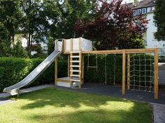 a wooden play set with a slide and climbing frame in front of a hedged area