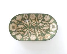 a green and gold plate with flowers on it's side, against a white background