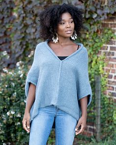 a woman standing in front of a brick wall wearing a blue ponchy sweater