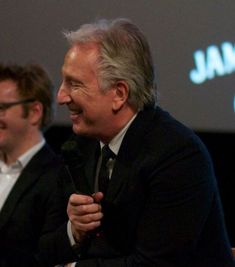 two men sitting next to each other in front of a projector screen and microphone