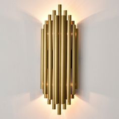 a wall mounted light that is on the side of a wall with gold tubes attached to it