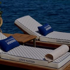 two mattresses sitting on top of a wooden dock next to the ocean with blue pillows