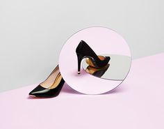 a pair of black high heeled shoes sitting on top of a mirror next to a pink wall