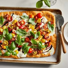 a square pizza with tomatoes, mozzarella and basil on it next to a bowl of sauce