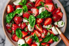 a bowl filled with strawberries and spinach on top of a marble countertop