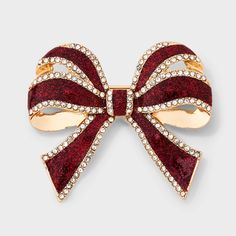 a red and gold bow brooch with crystal stones on the front, sitting on a white surface