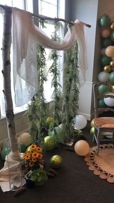 a room filled with balloons and greenery next to a tree in front of a window