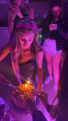 a girl in a tiara blows out candles on her birthday cake while others look on