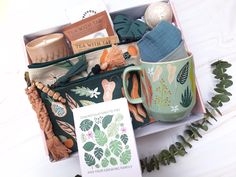 an open box containing tea, books, and other items on a white surface with greenery