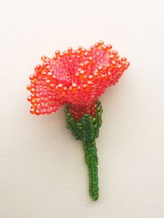 a beaded pink flower with green stems on a white surface, surrounded by beads