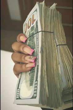 a woman's hand holding money in front of her face with pink nail polish