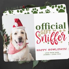 a white dog wearing a santa hat and holding a christmas ornament with paw prints on it