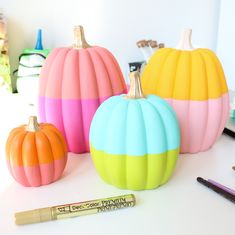 three painted pumpkins sitting on top of a table next to a marker and pen