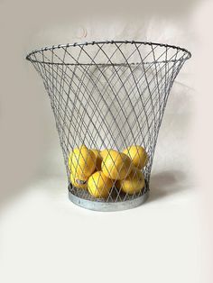 a wire basket filled with lemons on top of a white table