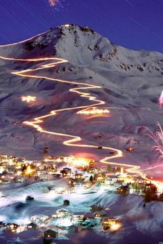 fireworks are lit up in the night sky over a town and mountain with snow on it