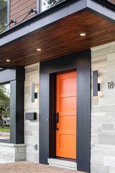 an orange door is on the side of a house with black trim and wood paneling