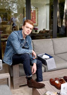 a young man sitting on top of a couch next to a shoe box and shoes