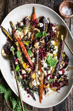 a white plate topped with carrots and other vegetables next to a spoon on top of a wooden table