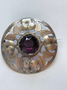 This is an absolutely stunning antique 1900 830 silver signed Danish brooch. The piece is signed 830 with the letter S as well as HNH connected. This is the hallmark for Hans Nicolajsen Hansen. The center of the brooch holds an amethyst crystal that measures 3/4 of an inch. The brooch measures 2 inches across. It has a classic early 1900s Victorian style pin with a classic C clasp.  The pin weighs 16.1 g. This item is an excellent preowned vintage condition with normal aging. The crystal is clean with minimal surface wear.  The pinpoint is sharp and moves easily. Vintage Gemstone Round Brooches, Vintage Silver Brooch With Gemstone, Vintage Silver Gemstone Brooch, Antique Hallmarked Purple Brooches, Victorian Antique Silver Brooches, Antique Round Brooch With Intricate Design, Victorian Antique Silver Brooches For Collectors, Antique Purple Hallmarked Brooches, Antique Round Brooches With Intricate Design