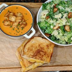 a bowl of soup and a sandwich on a cutting board next to a bowl of salad