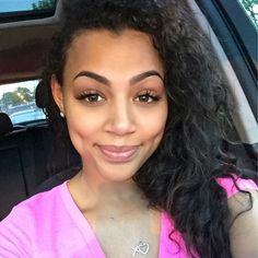 a woman sitting in the back seat of a car wearing a pink shirt and diamond necklace