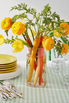 a vase filled with yellow flowers on top of a table next to plates and utensils