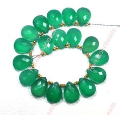 a green bracelet with gold beads and large tears on it's end is shown