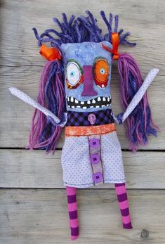 an odd looking doll with purple hair and orange eyes sitting on top of a wooden floor