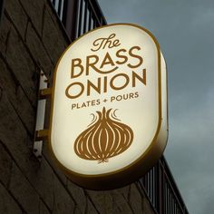 the brass onion sign is lit up on the side of a building with dark clouds in the background