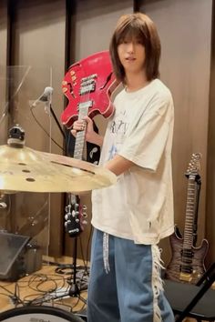 a young man holding a red guitar in front of a drum set and microphones