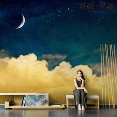 a woman sitting on a bench in front of a wall with clouds and the moon