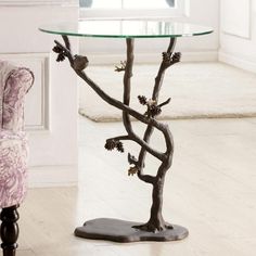 a glass table with branches and pine cones on it in front of a pink chair