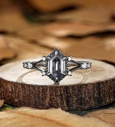 an engagement ring sitting on top of a piece of wood with leaves in the background