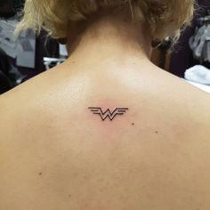 the back of a woman's neck with a small wonder logo tattoo on it