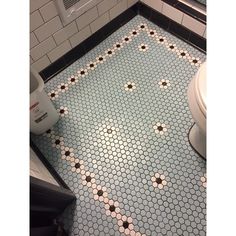 a white toilet sitting in a bathroom next to a tiled floor with black dots on it