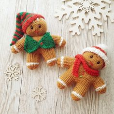 two small knitted gingerbread men are next to snowflakes on a wooden surface