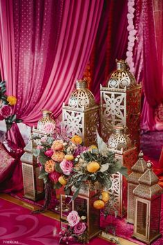 pink and gold wedding decor with lanterns and flowers on the table in front of red drapes