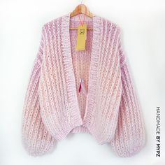 a pink cardigan sweater hanging on a hanger with a tag attached to it