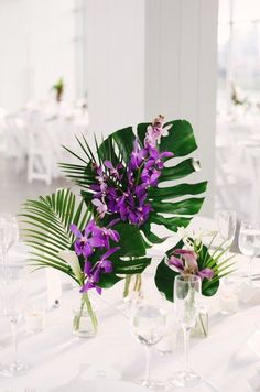 purple flowers and greenery in vases on a white table cloth with wine glasses