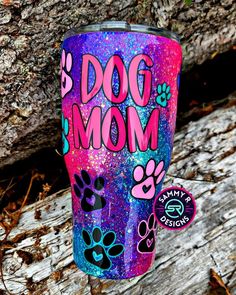 a pink and blue glitter tumbler with dog mom written on it next to a tree