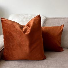 two orange pillows sitting on top of a couch next to a white furnishing