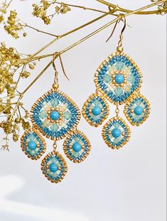 two pairs of blue and white earrings hanging from a branch with flowers in the background