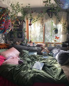 an unmade bed in a messy room with plants hanging from the ceiling and windows