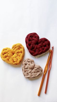 three crocheted hearts sitting on top of a white table next to knitting needles