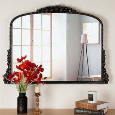 a mirror sitting on top of a table next to a vase filled with red flowers