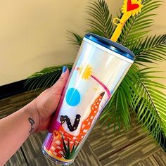 a person holding up a colorful cup with a yellow straw sticking out of it's side