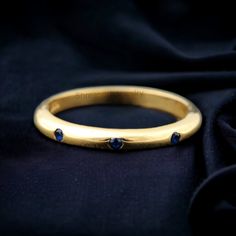 a gold ring with three blue stones on it's side, sitting on a black cloth