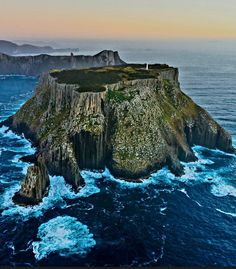 an island in the middle of the ocean with waves crashing around it and some rocks sticking out of the water